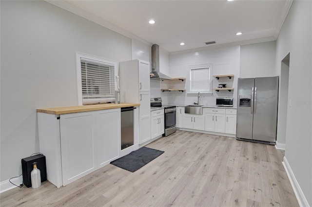 kitchen featuring wall chimney exhaust hood, stainless steel appliances, crown molding, butcher block countertops, and white cabinetry