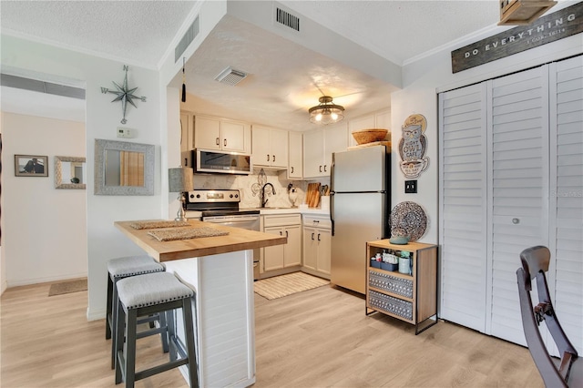 kitchen with light wood-type flooring, a breakfast bar area, a textured ceiling, and appliances with stainless steel finishes