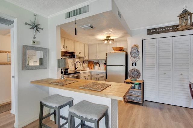 kitchen with a breakfast bar area, a textured ceiling, appliances with stainless steel finishes, kitchen peninsula, and light hardwood / wood-style floors