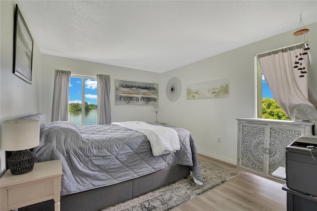 bedroom with a water view, access to exterior, a textured ceiling, and light hardwood / wood-style flooring