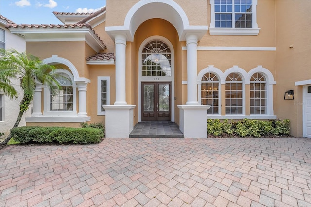 view of exterior entry featuring stucco siding, a tiled roof, and french doors