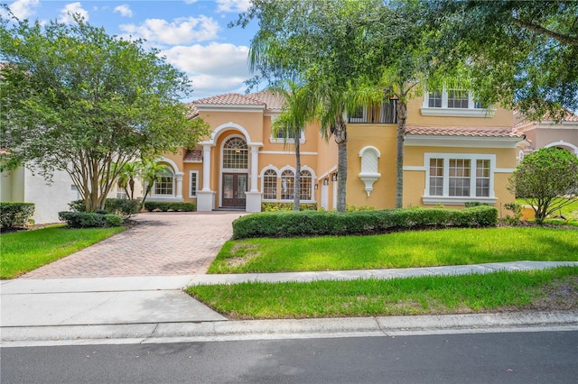 mediterranean / spanish-style house featuring a front yard, decorative driveway, a tile roof, and stucco siding