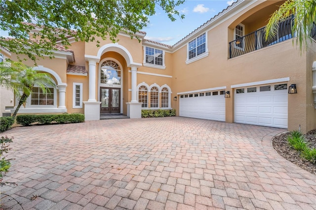 view of front of home with decorative driveway, french doors, a tile roof, stucco siding, and an attached garage