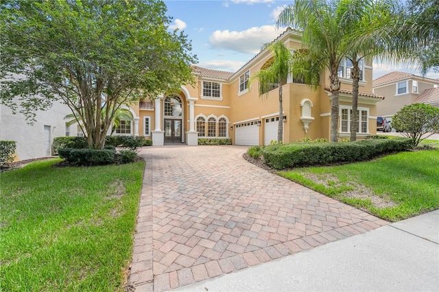 view of front of home with an attached garage, a tiled roof, decorative driveway, stucco siding, and a front lawn