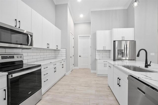 kitchen with light stone counters, stainless steel appliances, backsplash, white cabinets, and a sink