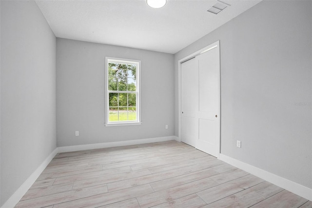 unfurnished bedroom with light wood-type flooring, baseboards, visible vents, and a closet