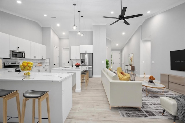 kitchen featuring ornamental molding, a breakfast bar, a kitchen island with sink, stainless steel appliances, and high vaulted ceiling