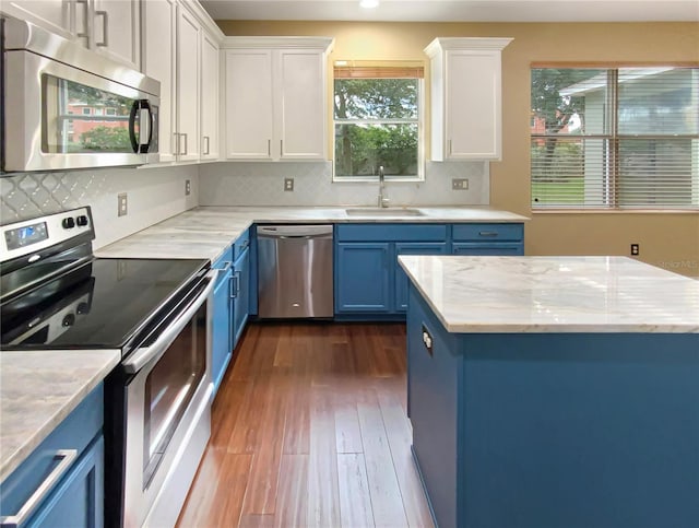 kitchen with stainless steel appliances, white cabinetry, blue cabinets, and backsplash