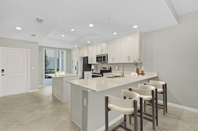 kitchen featuring kitchen peninsula, appliances with stainless steel finishes, sink, white cabinetry, and a breakfast bar area