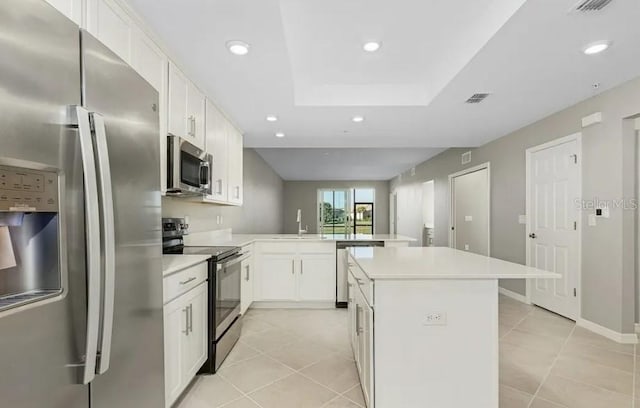 kitchen featuring kitchen peninsula, appliances with stainless steel finishes, light tile patterned floors, white cabinets, and a center island