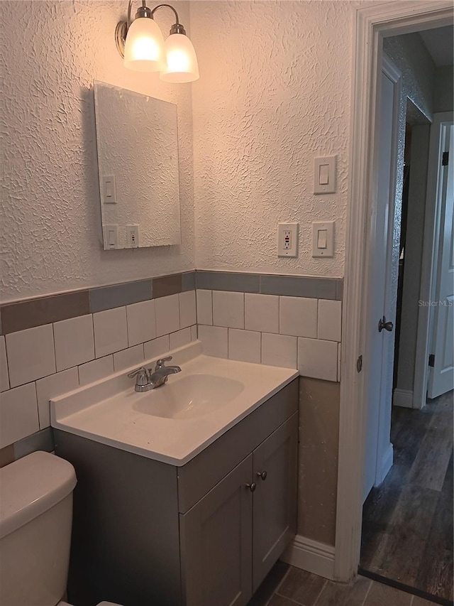 bathroom with hardwood / wood-style floors, tile walls, backsplash, vanity, and toilet