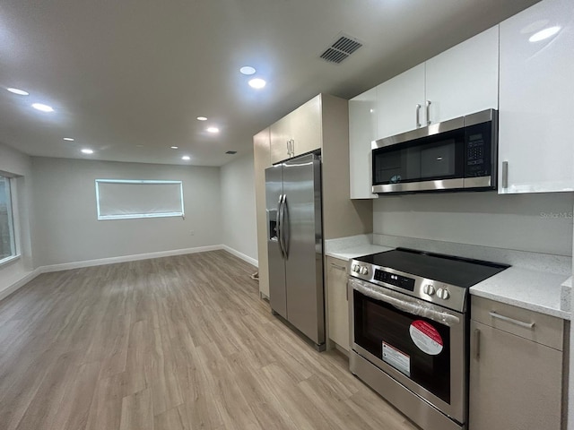 kitchen with white cabinetry, light stone counters, light wood-type flooring, and stainless steel appliances