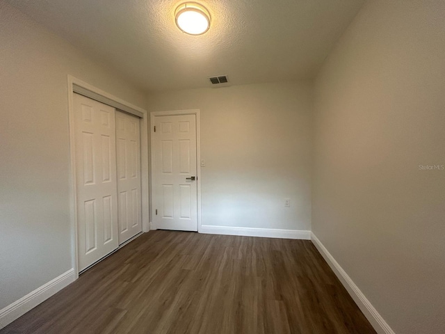 unfurnished bedroom with dark hardwood / wood-style floors, a textured ceiling, and a closet