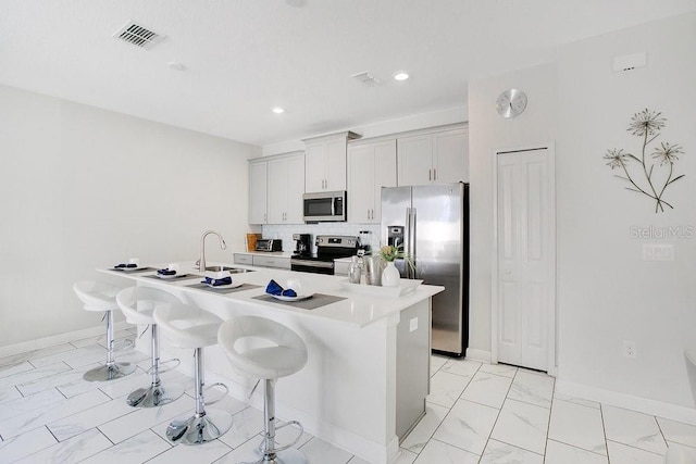 kitchen with sink, a kitchen island with sink, white cabinetry, appliances with stainless steel finishes, and a kitchen breakfast bar