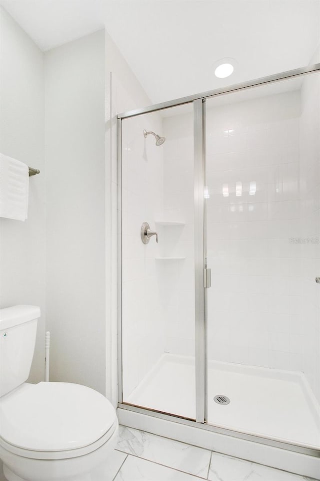 bathroom featuring a shower with door and toilet