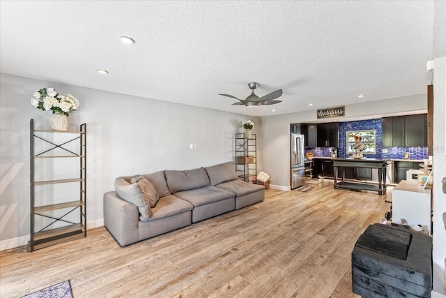 living room with ceiling fan, a textured ceiling, and light hardwood / wood-style flooring