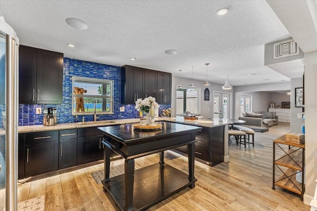 kitchen featuring a kitchen breakfast bar, backsplash, sink, light hardwood / wood-style floors, and hanging light fixtures