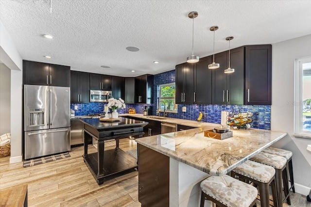 kitchen with sink, appliances with stainless steel finishes, decorative light fixtures, light stone counters, and kitchen peninsula