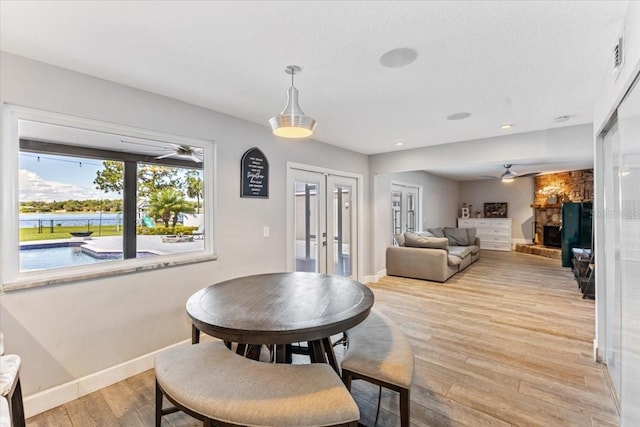 dining area featuring a fireplace, ceiling fan, light hardwood / wood-style flooring, and french doors