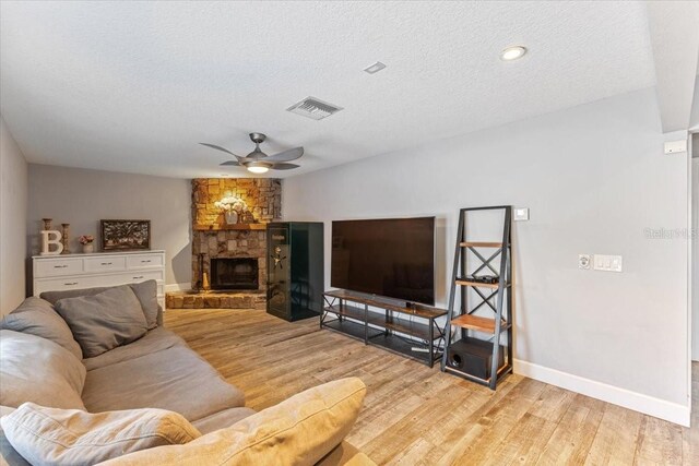 living room featuring a fireplace, a textured ceiling, light wood-type flooring, and ceiling fan