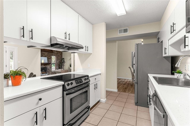 kitchen with sink, light tile patterned flooring, appliances with stainless steel finishes, a textured ceiling, and white cabinets