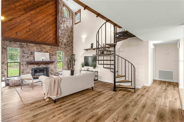 living room featuring plenty of natural light, light hardwood / wood-style flooring, a stone fireplace, and high vaulted ceiling