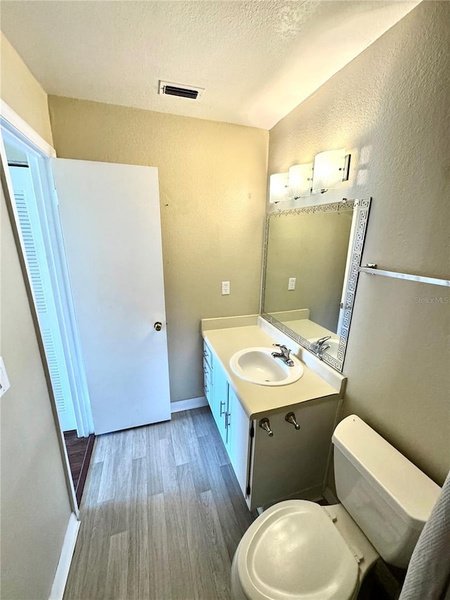 bathroom featuring toilet, a textured wall, visible vents, and wood finished floors