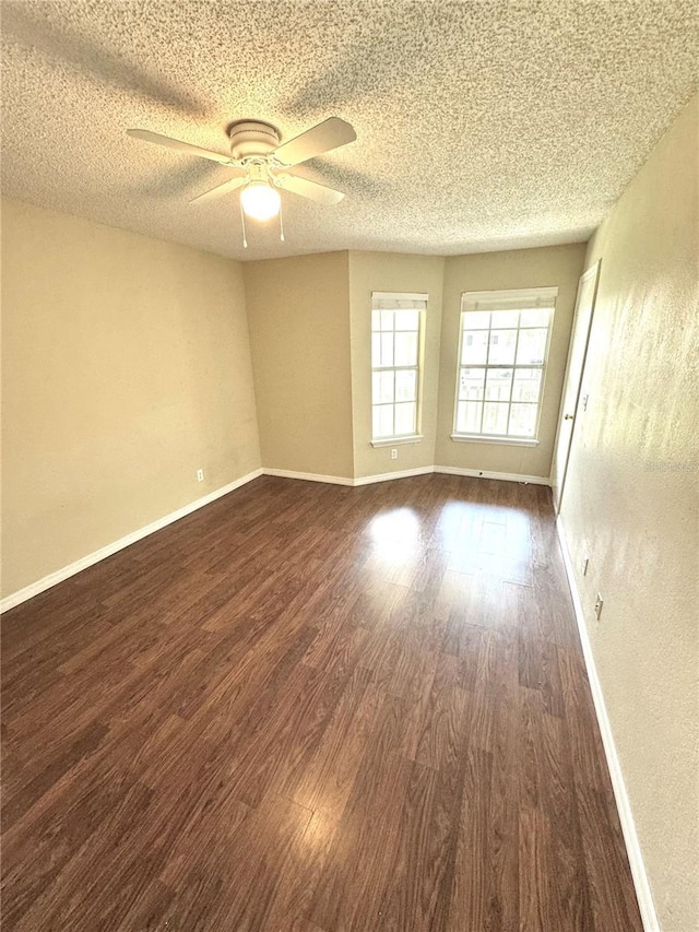 spare room with baseboards, a ceiling fan, dark wood-style flooring, and a textured ceiling