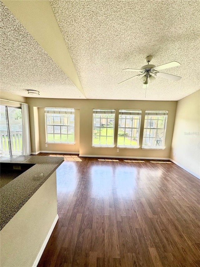 unfurnished living room featuring a textured ceiling, baseboards, and dark wood-type flooring