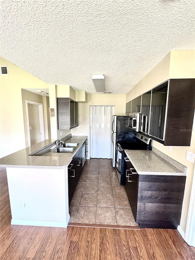 kitchen featuring a sink, light countertops, stainless steel appliances, a peninsula, and wood finished floors
