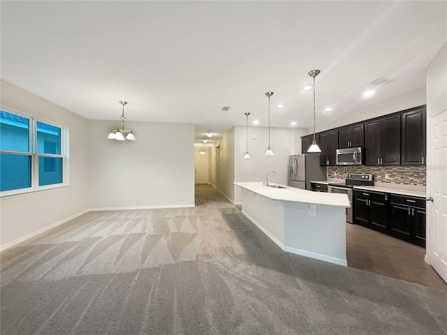 kitchen with backsplash, sink, hanging light fixtures, an island with sink, and stainless steel appliances