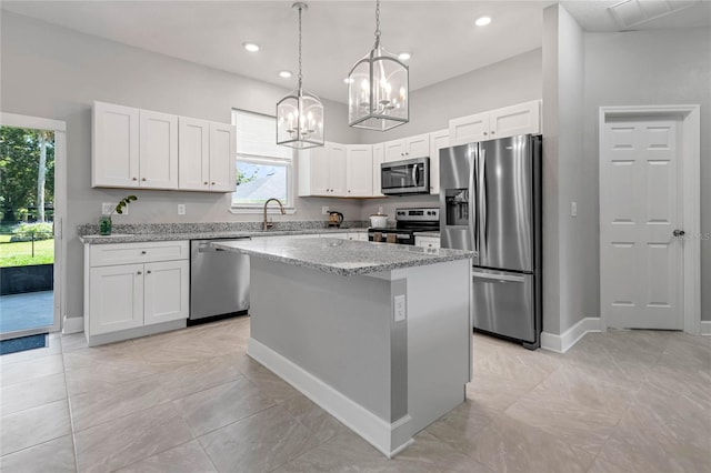 kitchen featuring white cabinets, light stone countertops, appliances with stainless steel finishes, decorative light fixtures, and a kitchen island