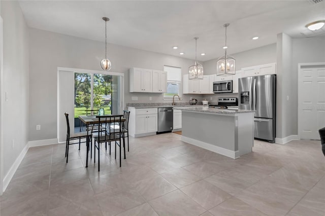 kitchen featuring light stone countertops, appliances with stainless steel finishes, decorative light fixtures, white cabinets, and a center island