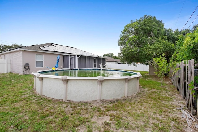 rear view of house featuring a lawn, solar panels, and a fenced in pool