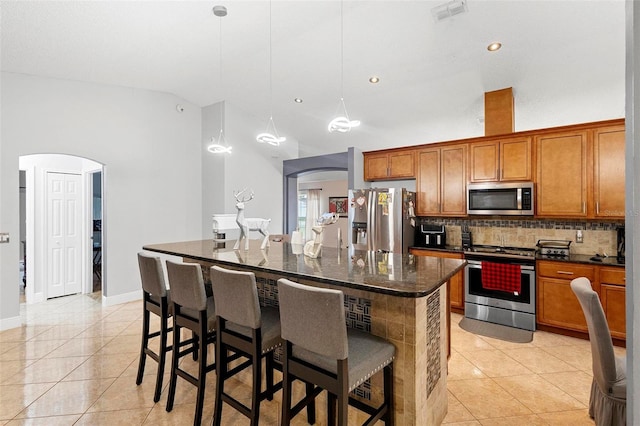 kitchen with a breakfast bar, hanging light fixtures, an island with sink, stainless steel appliances, and light tile patterned floors