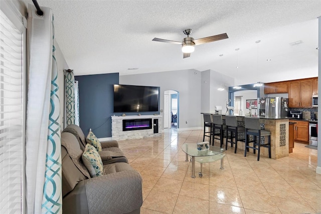 living room with ceiling fan, a textured ceiling, a stone fireplace, and a healthy amount of sunlight