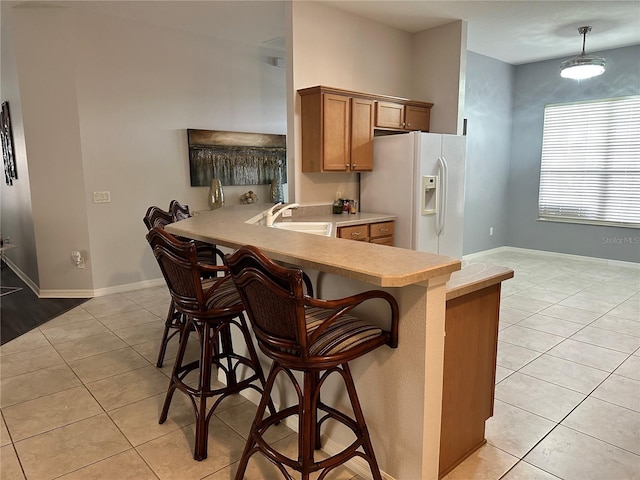 kitchen with sink, white refrigerator with ice dispenser, kitchen peninsula, a kitchen bar, and light tile patterned floors