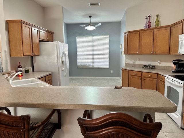 kitchen featuring kitchen peninsula, a kitchen breakfast bar, white appliances, sink, and light tile patterned flooring