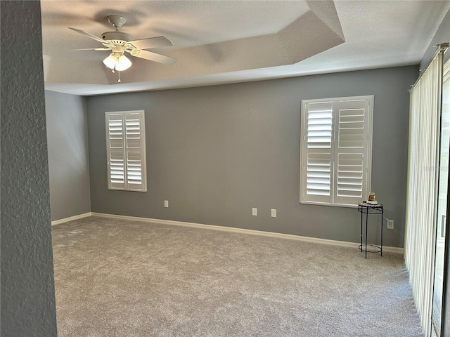 carpeted spare room with ceiling fan, a textured ceiling, and a tray ceiling