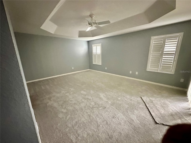 carpeted spare room with a raised ceiling and ceiling fan