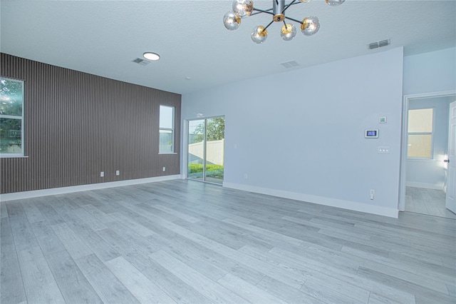 unfurnished room with a notable chandelier, light wood-type flooring, and a textured ceiling