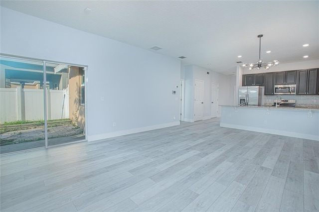 unfurnished living room with sink, a chandelier, and light wood-type flooring