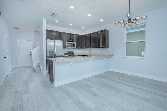 kitchen with appliances with stainless steel finishes, hanging light fixtures, kitchen peninsula, a kitchen bar, and decorative backsplash