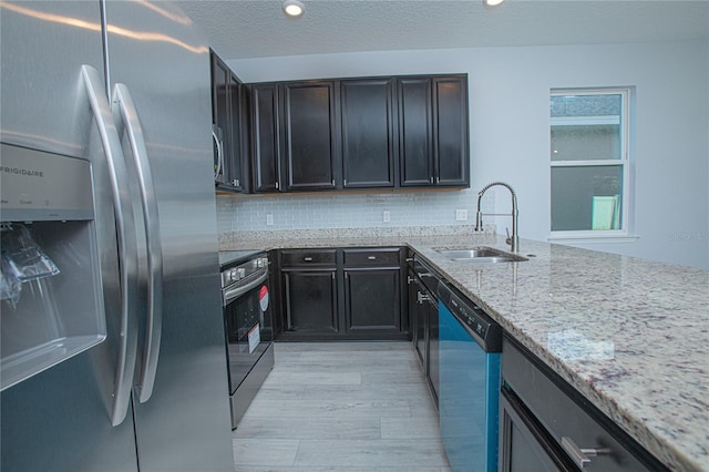 kitchen with stainless steel appliances, sink, a textured ceiling, decorative backsplash, and light stone countertops