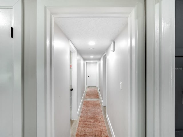 hallway with a textured ceiling and baseboards