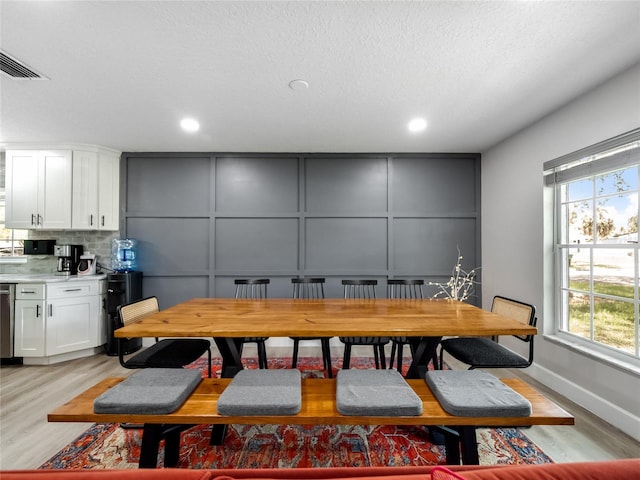 dining area with visible vents, a decorative wall, a textured ceiling, and light wood finished floors