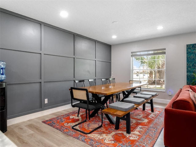 dining room featuring light wood-type flooring, a decorative wall, a textured ceiling, and recessed lighting