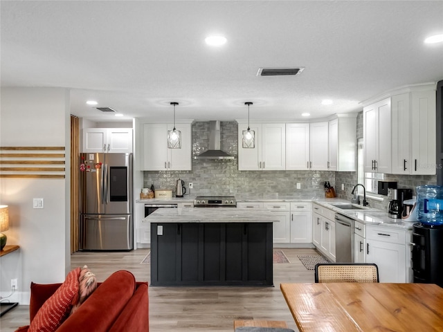 kitchen with stainless steel appliances, tasteful backsplash, white cabinetry, a sink, and wall chimney exhaust hood