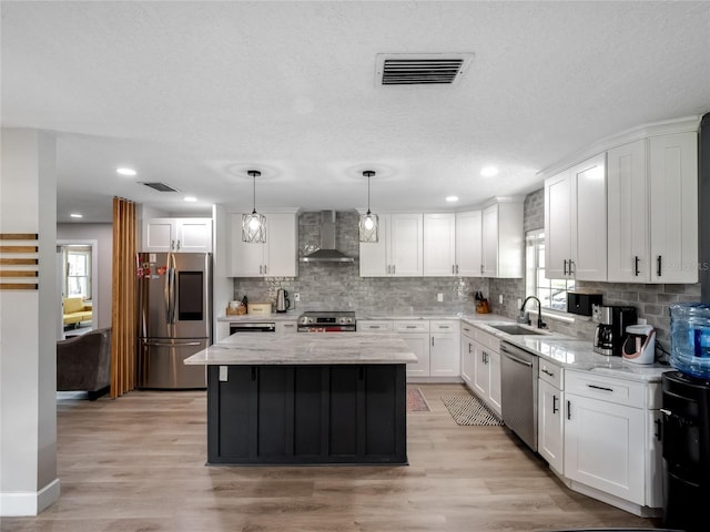 kitchen featuring wall chimney exhaust hood, appliances with stainless steel finishes, a sink, and visible vents