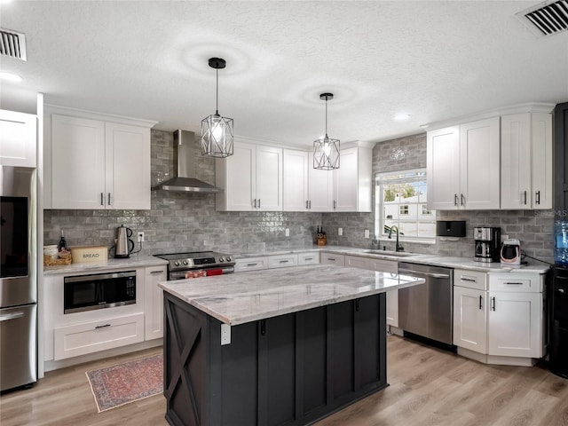 kitchen with stainless steel appliances, visible vents, light wood-style floors, a sink, and wall chimney range hood